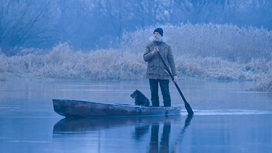 Kadr z filmu W trosce o bagna. Wioślarz z psem na łódce.